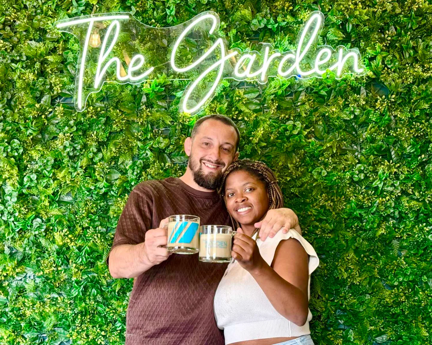Leo and Brittani smiling together in front of The Garden's lush plant wall