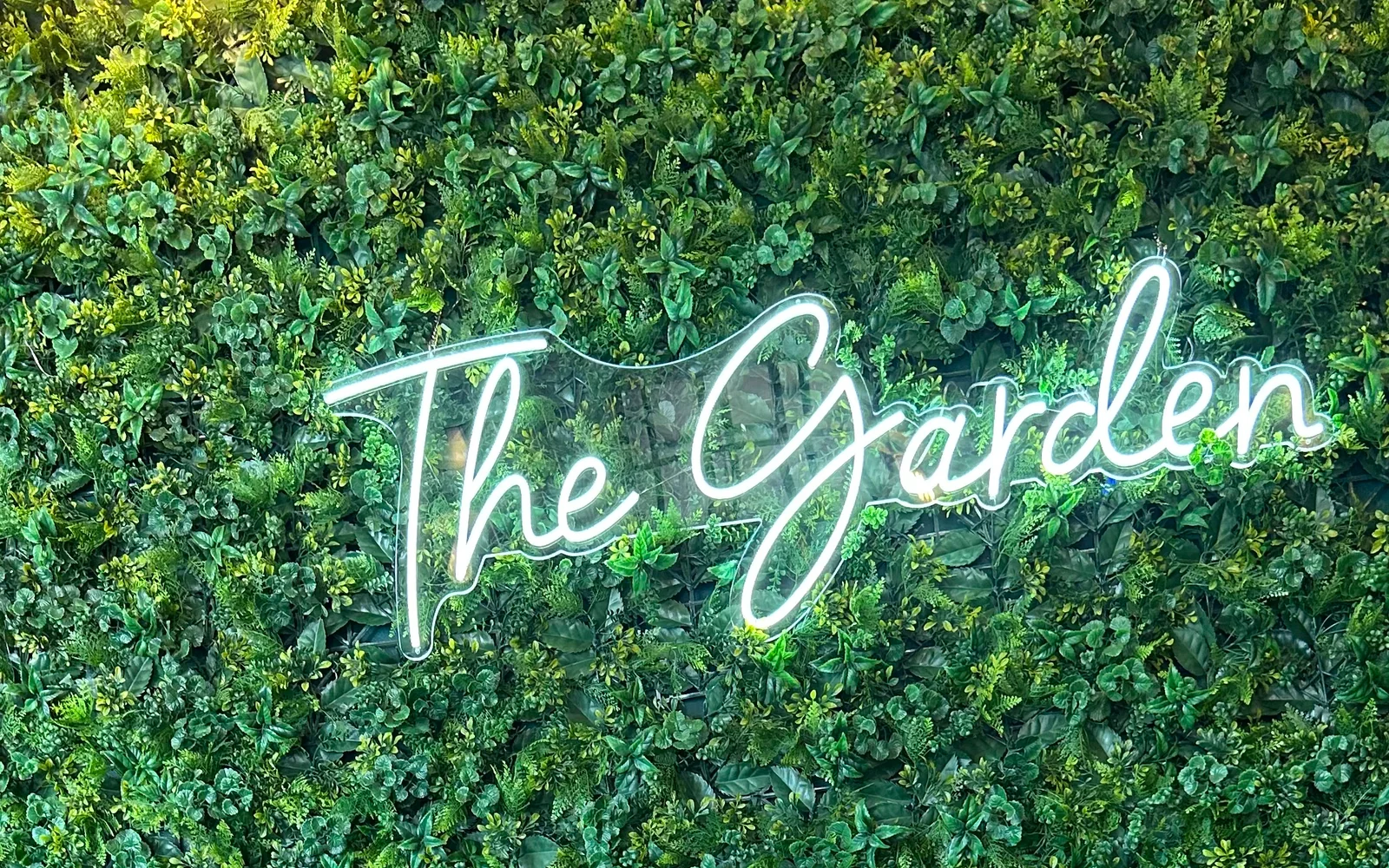 The Garden neon sign glowing over botanical plant greenery